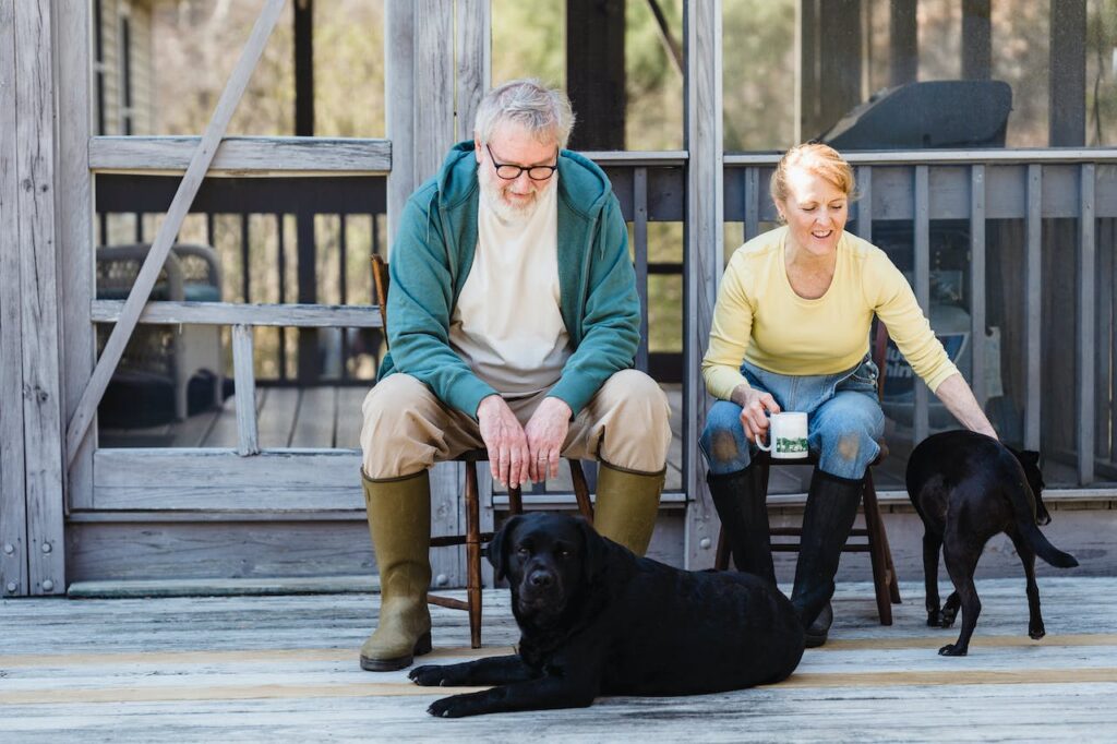 Elderly couple with dogs sitting on back porch.